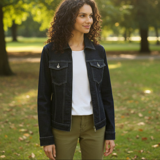 Woman wearing a dark denim jacket over a white shirt with green pants on a light background
