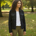 Woman wearing a dark denim jacket over a white shirt with green pants on a light background